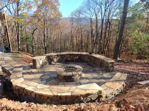 Circular flagstone patio with a fire pit and curved seating wall by F. Stone Designs