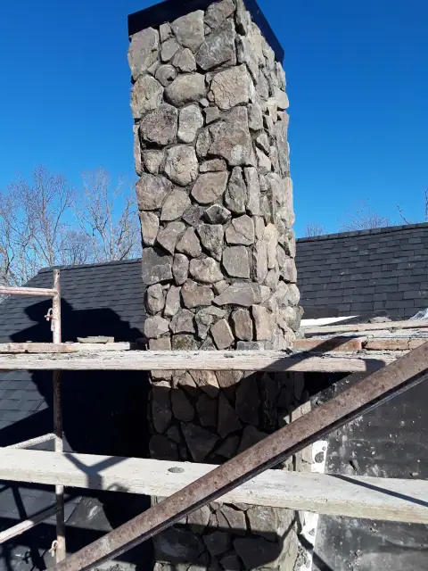 Stone chimney under construction with roof scaffolding