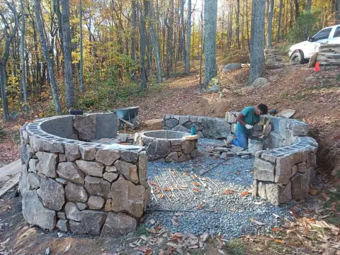 Stone patio and curved seating walls under construction by F. Stone Designs